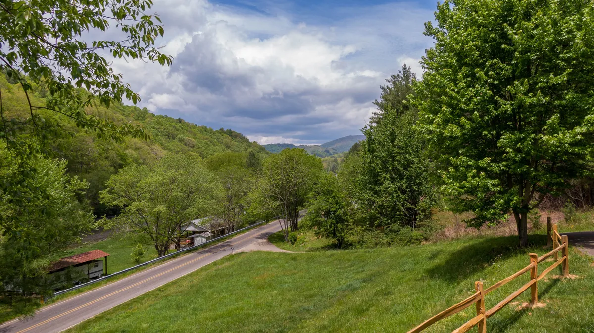 A panoramic view of rolling hills, a quiet country road, and a scattering of buildings under a cloudy sky. The landscape offers a sense of openness and the promise of outdoor adventure.