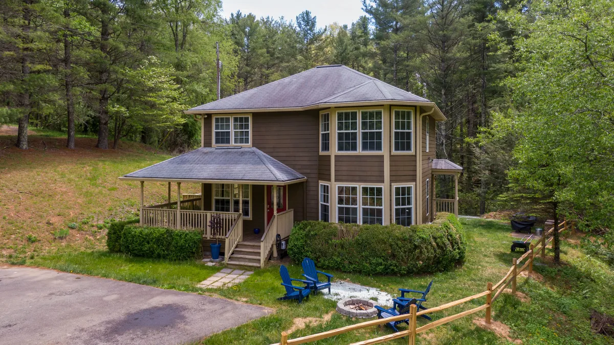 A welcoming, cozy exterior shot featuring the house, a spacious yard, a fire pit, and comfortable outdoor seating. The scene suggests a space designed for family gatherings, relaxation, and evening campfires.