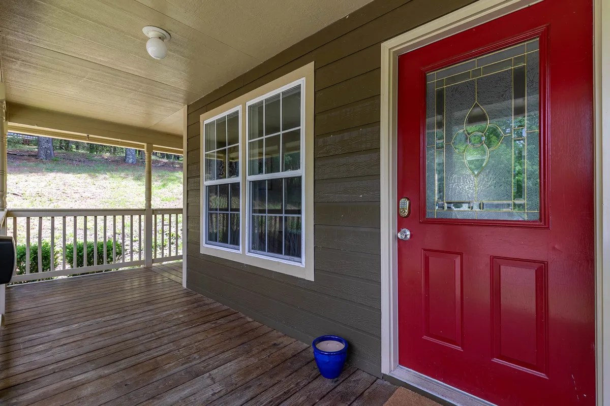 The image shows a vibrant red front door set in a wooden porch with stained glass and classic features, hinting at the blend of charm and comfort that guests experience on arrival. Natural light, exterior textures, and visible porch space evoke a sense of hospitality and the transition between indoor and outdoor living.