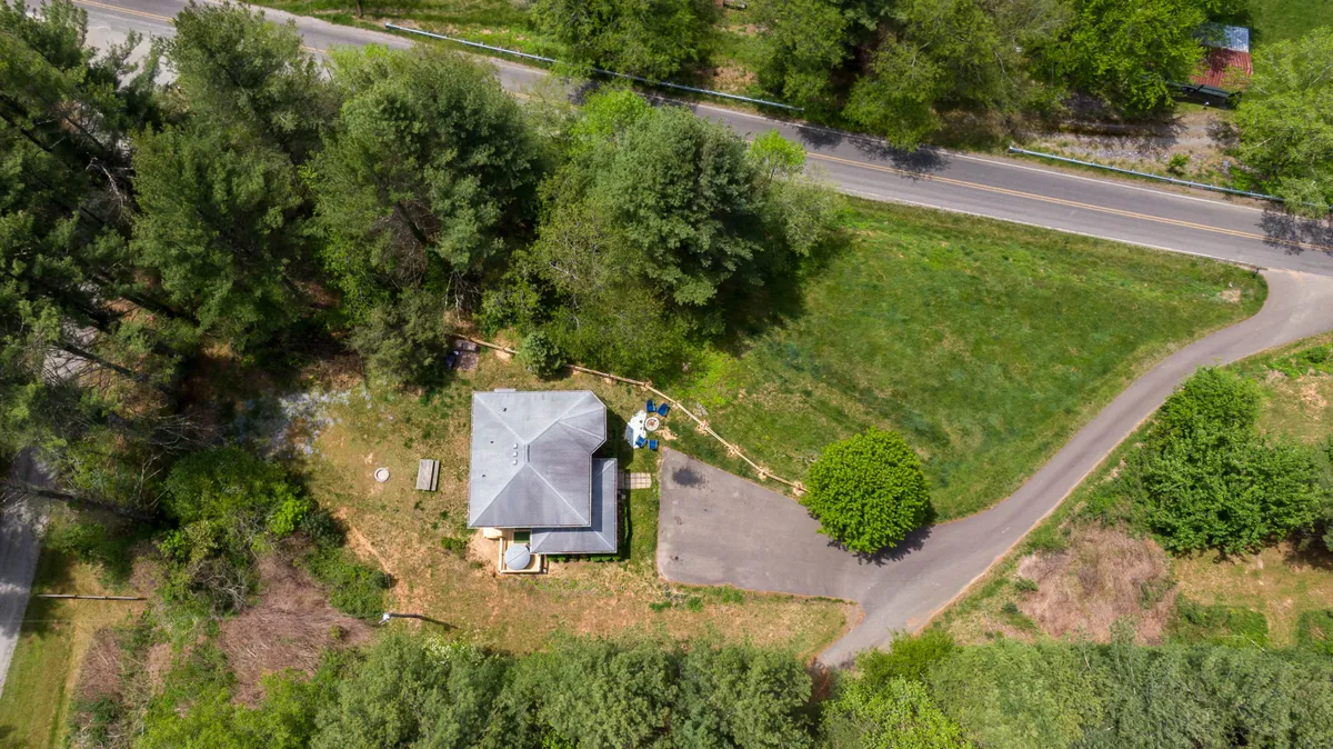 This image captures the house nestled among tall trees, with a welcoming porch and driveway leading up to the entrance. The surrounding greenery emphasizes the peaceful, nature-immersed setting.