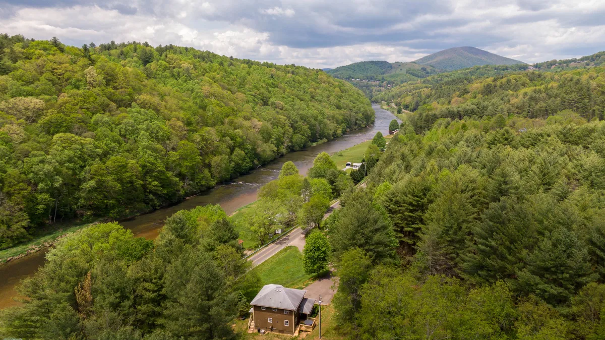 This exterior image showcases the house situated right next to the river, surrounded by lush trees and natural scenery. The tranquil water is visible in the foreground, emphasizing the property’s direct river access and the beauty of its natural surroundings.