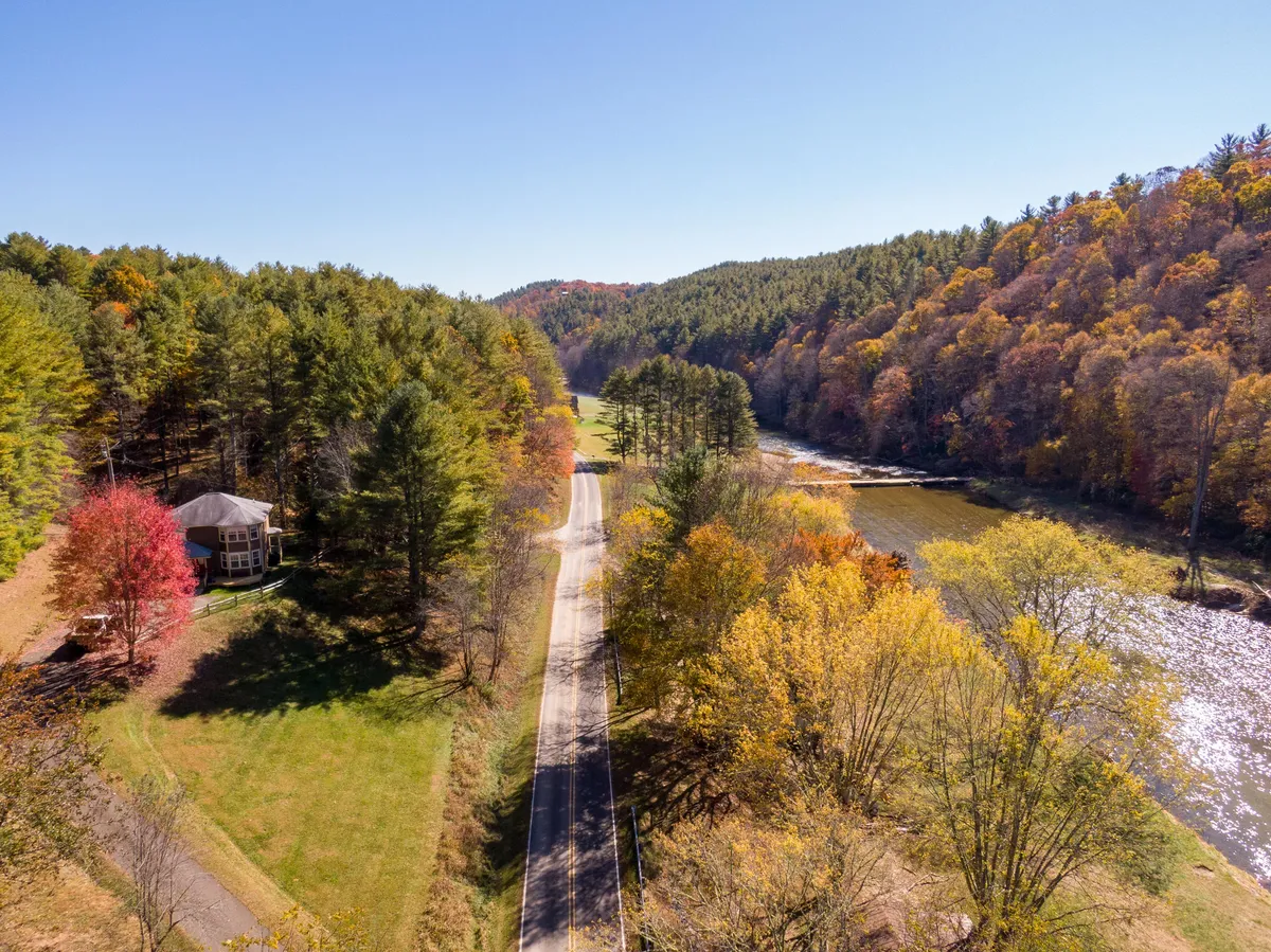 An elevated view showcases the home nestled among tall trees, with a winding river and quiet road nearby. The surrounding natural landscape emphasizes the home's access to scenic trails, water activities, and the tranquil environment described in the section.