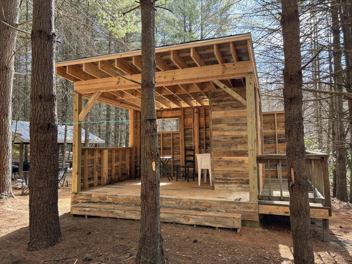 This image captures a cozy wooden patio area surrounded by mature trees, seamlessly blending the home's exterior with its natural environment. The inviting patio space offers ample room for relaxing outdoors, dining, or letting pets enjoy the fresh air. The visible structure and surrounding greenery highlight a sense of privacy and freedom.