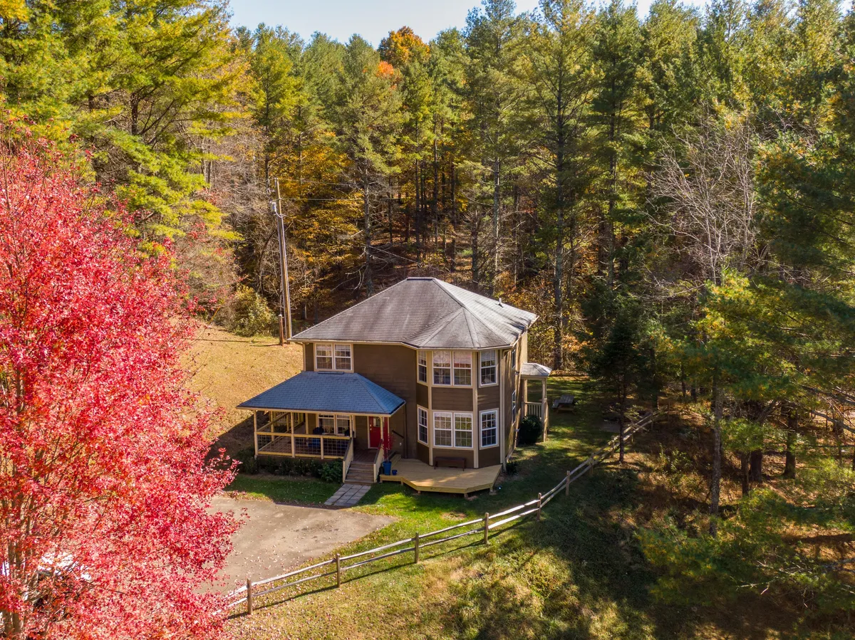 A wide exterior image of the house with surrounding trees and colorful foliage, evoking a sense of adventure and nature. The porch and yard are visible, suggesting space for both relaxation and outdoor activities.