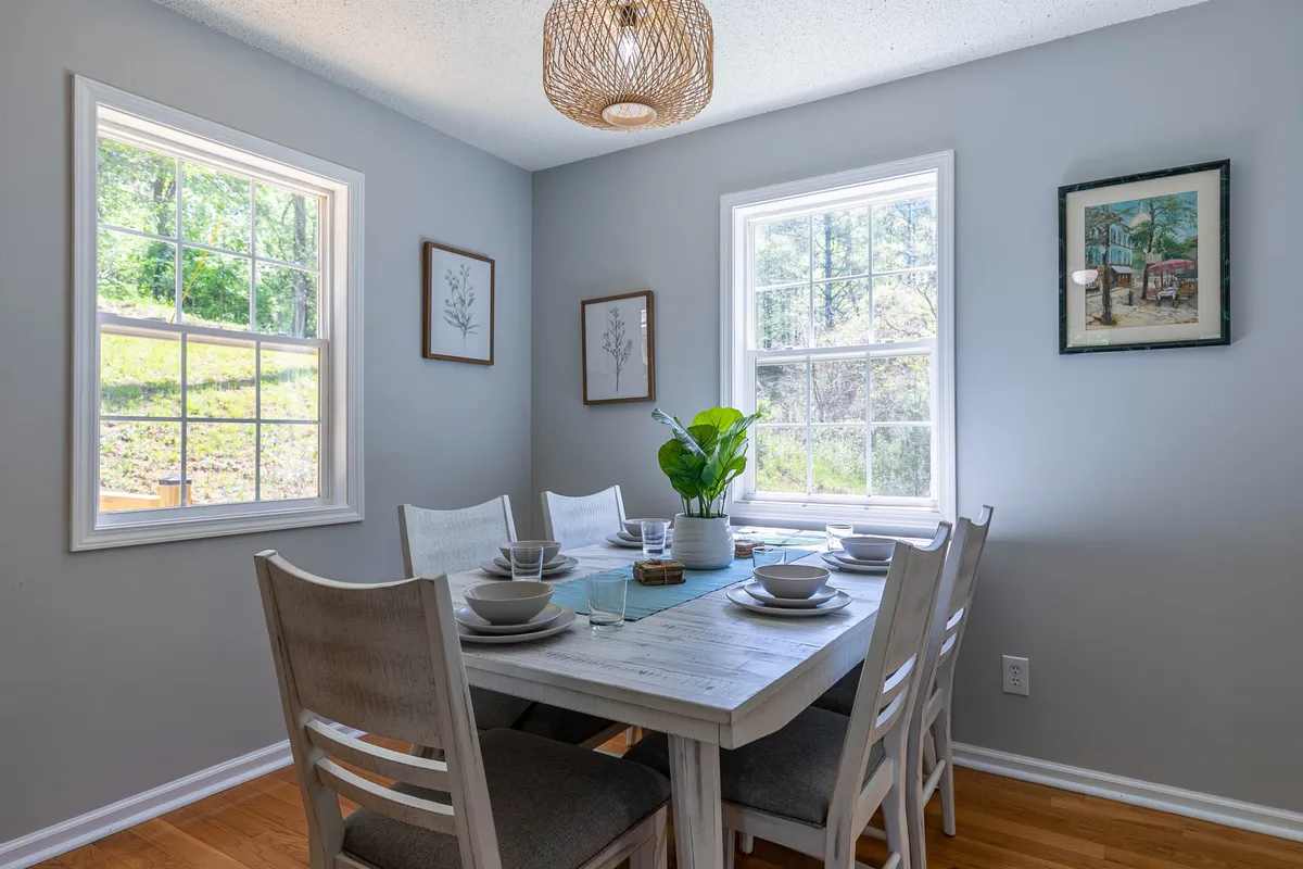A bright, airy corner with a dining table, large windows, a leafy plant, and a stylish light fixture. The space feels perfect for working from home, enjoying meals, or planning adventures, emphasized by the ample natural light and inviting decor.